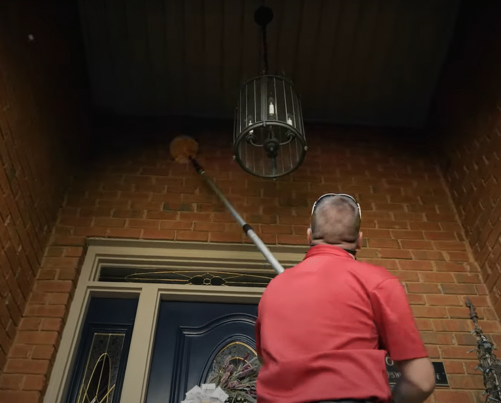 Pest control specialist removing cobwebs near a front entryway during Pest Control in East Lansing service.”