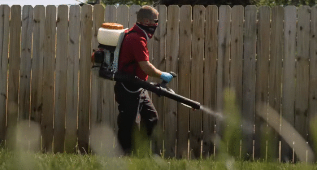 Technician spraying a backyard fence line as part of outdoor Pest Control in East Lansing.